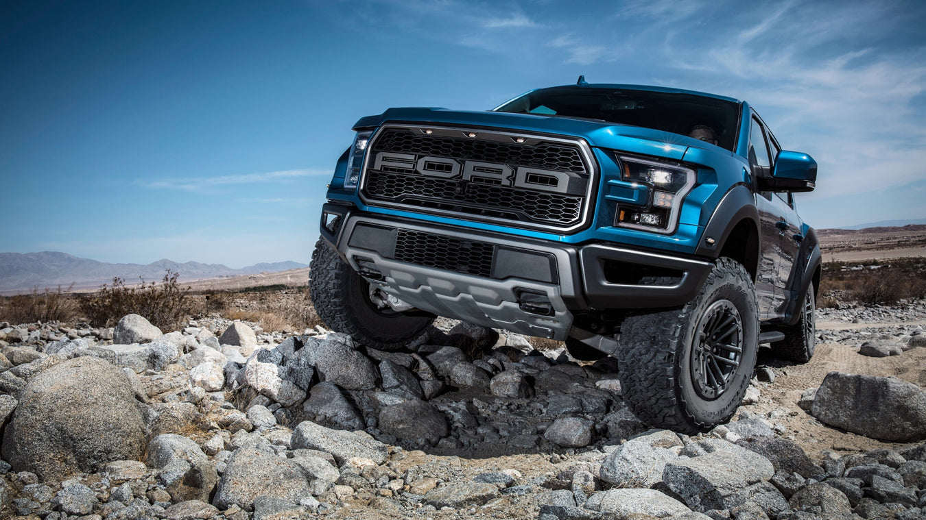 Blue pickup poised on a rocky terrain.  The truck appears to have a raised suspension and off-road tires, indicating its equipped for rugged landscapes.